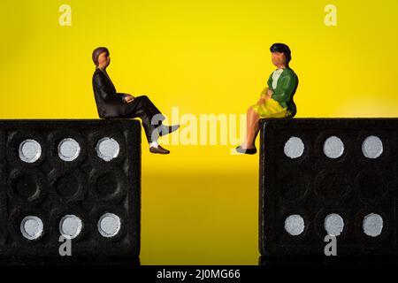 Geschäftsmann und -Frau sitzen auf Domino-Token Gelber Hintergrund Stockfoto