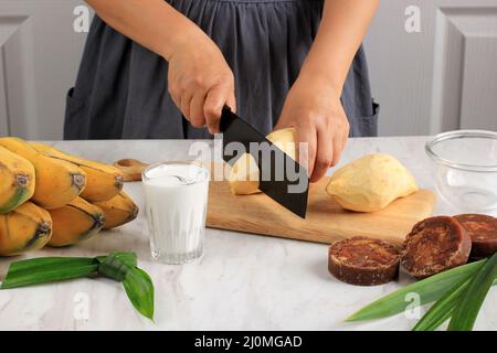 Schneiden von Süßkartoffeln, Zubereiten von Bananenkartoffeln (Kolak Pisang Ubi). Reife Banane, Süßkartoffeln, Palmzucker (Gula Merah), Pandan Le Stockfoto