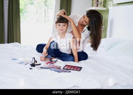 Mama ist meine persönliche Stylistin. Aufnahme einer Mutter, die ihre kleinen Töchter beim Spielen mit Make-up zu Hause mit Haaren stylt. Stockfoto