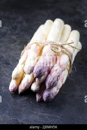 Roher weißer Spargel mit violettem Kopf als Bund auf einem alten rustikalen Metallbrett als Nahaufnahme Stockfoto