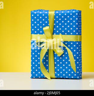 Box verpackt in festliches blaues Papier und gebunden mit Seide gelben Band auf einem gelben Hintergrund, Geburtstagsgeschenk, Überraschung Stockfoto