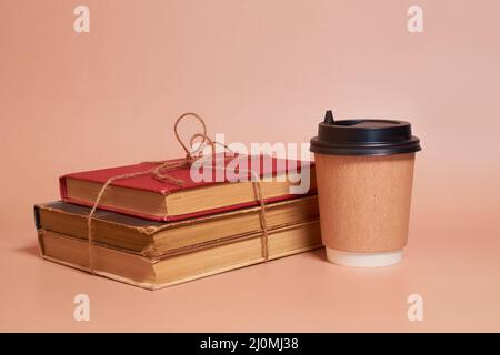 Eine Papptasse Kaffee steht neben einem Stapel alter Bücher, gefesselt mit einem Juteseil Stockfoto