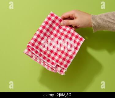 Weibliche Hand mit rot-weißer Textilserviette auf grünem Hintergrund Stockfoto