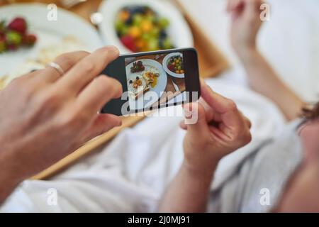 Sehen Sie sich dieses fantastische Frühstück an, das Sie gemacht haben. Pov-Aufnahme eines unverkennbaren Paares, das ein Foto ihres Frühstücks gemacht hat, das sie während des Frühstücks im Bett hatten Stockfoto