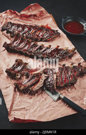 Gegrillte Schweinelende-Rippen St. Louis, geschnitten mit heißer Honig-Chili-Marinade, serviert als Nahaufnahme auf Metzgerpapier Stockfoto