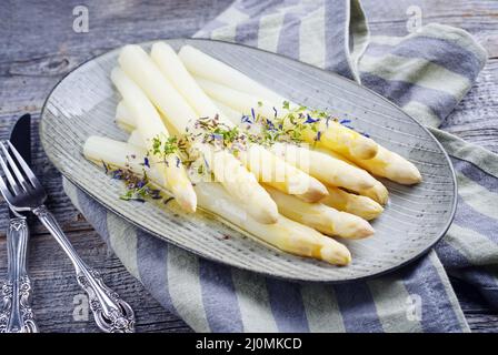 Traditioneller gedämpfter weißer Spargel im modernen Stil, garniert mit Buttersauce und Kräutern, serviert als Nahaufnahme auf einem Design-Teller Stockfoto