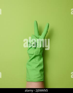Hand in einem grünen Gummihandschuh zum Reinigen auf grünem Hintergrund wird ein Teil des Körpers angehoben Stockfoto