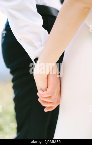 Die Hand des Bräutigams in einem weißen Hemd und einer schwarzen Hose hält die Hand der Braut in einem weißen Kleid. Nahaufnahme Stockfoto