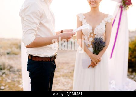 Sibenik, Kroatien - 05.06.17: Der Bräutigam hält ein Blatt Papier vor sich. Lächelnde Braut mit Lavendel-Bouquet steht in der Nähe. Cl Stockfoto