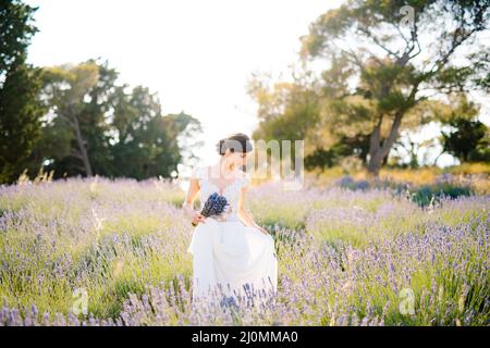 Sibenik, Kroatien - 05.06.17: Die Braut in einem weißen Spitzenkleid hält den Saum des Kleides mit einer Hand und hält einen Strauß Lavendel Stockfoto