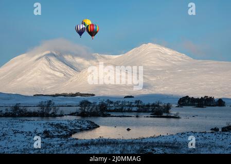 Digitales Composite-Bild von Heißluftballons, die im Winter über eine wunderschöne Landschaft fliegen und über Lochan Na h-Achlaise in Richtung Bergkette blicken Stockfoto