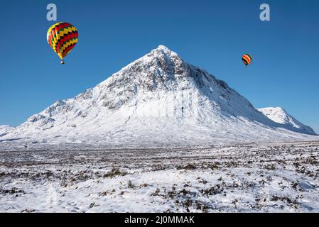 Digitales Composite-Bild von Heißluftballons, die über eine atemberaubende, ikonische Landschaft fliegen Winterbild des Berges Stob Dearg Buachaille Etive Mor in Schottland Stockfoto