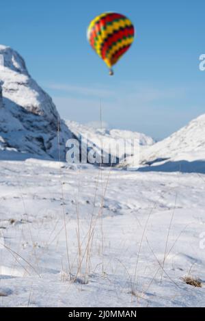 Digitales Composite-Bild von Heißluftballons, die über eine atemberaubende, ikonische Landschaft fliegen Winterbild des Berges Stob Dearg Buachaille Etive Mor in Schottland Stockfoto