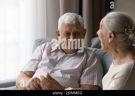 Ein älteres Paar, das sich auf dem Sofa entspannt, lacht und redet, fühlt sich glücklich Stockfoto
