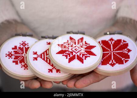 Frau hält Hand gemacht Kreuz Stich Folk Weihnachtsdekoration Schmuck Stickerei auf Sperrholz. Nordische Schneeflocken. Stockfoto