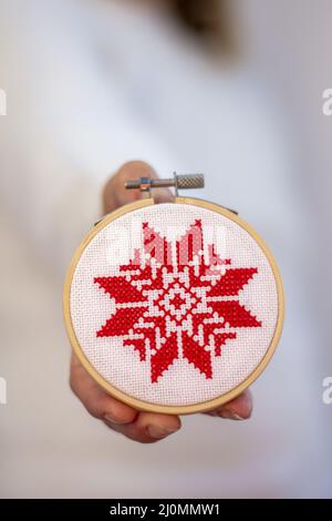 Frau hält Hand gemacht Kreuz Stich Folk Weihnachtsdekoration Schmuck Stickerei auf Sperrholz. Nordische Schneeflocken. Stockfoto