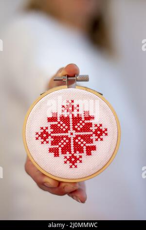 Frau hält Hand gemacht Kreuz Stich Folk Weihnachtsdekoration Schmuck Stickerei auf Sperrholz. Nordische Schneeflocken. Stockfoto