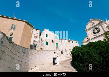 Sibenik, Kroatien - 05.06.17: Braut und Bräutigam, die Hände haltend, steigen die Stufen entlang der Kathedrale des heiligen Jakobus in Sibenik, Kroate Stockfoto