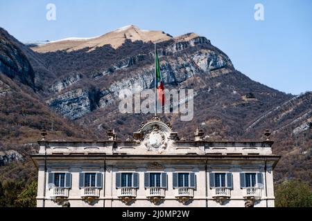 Flagge über der Villa Sola Cabiati im Hintergrund der Berge. Comer See, Italien Stockfoto