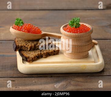 Kaviar aus rotem Lachs liegt auf einem Stück Roggenbrot. Brauner Holztisch Stockfoto