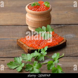 Kaviar aus rotem Lachs liegt auf einem Stück Roggenbrot. Brauner Holztisch Stockfoto