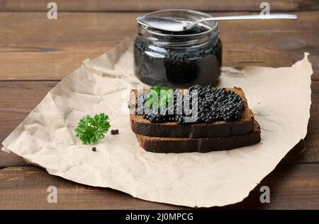 Sandwich mit schwarzem Kaviar auf einer Scheibe Roggenbrot und einem Glas mit einem Löffel, ein köstlicher Snack auf dem Tisch Stockfoto