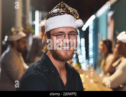 Im der junge Weihnachtsmann. Porträt eines fröhlichen jungen Mannes, der während der weihnachtszeit zu Hause einen festlichen Hut trägt. Stockfoto