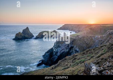 Blick auf den Sonnenuntergang über den Küstenklippen von Kynance Cove in Cornwall, England. Stockfoto