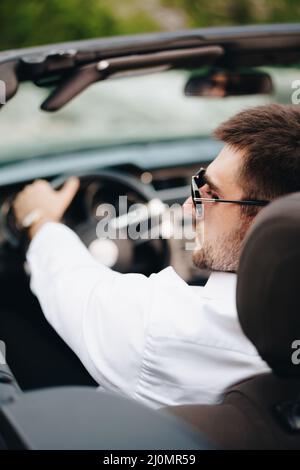 Der Mann in weißem Hemd sitzt in Nahaufnahme hinter dem Steuer eines offenen Autos Stockfoto