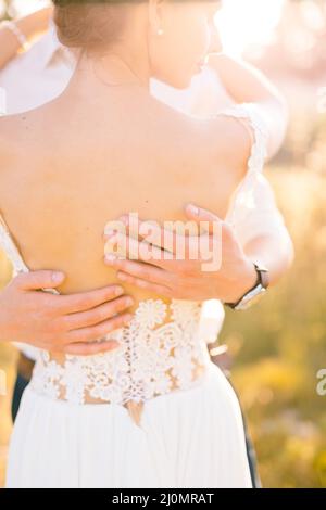 Sibenik, Kroatien - 05.06.17: Die Hände des Bräutigams umarmen den Rücken der Braut in einem weißen Spitzenkleid. Nahaufnahme Stockfoto