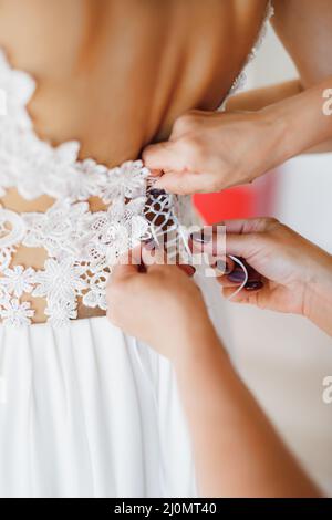 Damenhänden schnüren das Spitzenkorsett des Brautkleides. Nahaufnahme Stockfoto