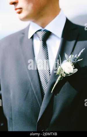 Bräutigam in einer schwarzen Jacke, einem weißen Hemd, einer gepunkteten Krawatte mit einem Boutonniere. Nahaufnahme Stockfoto