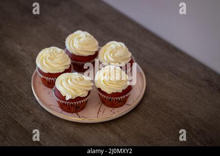 Fünf hausgemachte Cupcakes aus rotem Samt mit Frischkäse auf einem Teller auf einem Holztisch Stockfoto