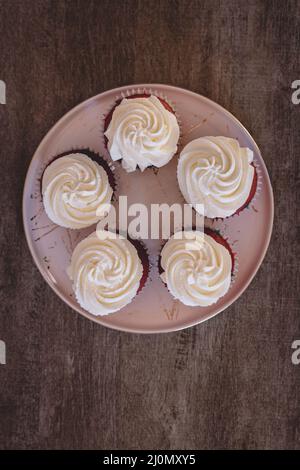 Fünf hausgemachte Cupcakes aus rotem Samt mit Frischkäse auf einem Teller auf einem Holztisch Stockfoto