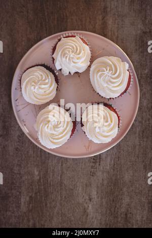 Fünf hausgemachte Cupcakes aus rotem Samt mit Frischkäse auf einem Teller auf einem Holztisch Stockfoto