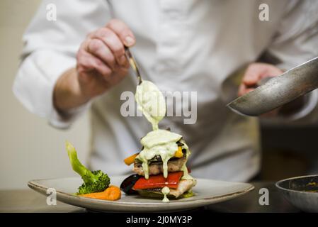 Koch gießt Saucenmahlzeit ein Stockfoto