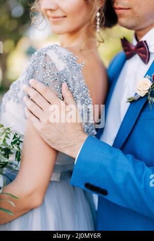 Kotor, Montenegro - 08.06.17: Bräutigam in einem blauen Anzug umarmt die Braut mit einem Blumenstrauß an den Schultern. Nahaufnahme Stockfoto