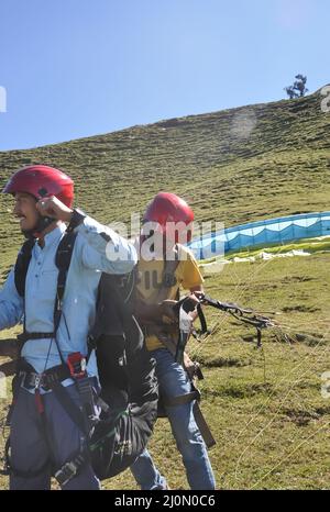 Mandi, Himachal Pradesh, Indien - 10 16 2021: Gleitschirmflieger helfen einem Touristen bei der Anpassung des Fallschirms an die Vorbereitung auf das Gleitschirmfliegen Stockfoto