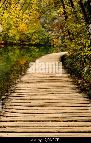 Eine rustikale Holzpromenade, die entlang des Ufers eines malerischen Bergsees mit Bäumen und Laub in intensiven Herbstfarben führt Stockfoto