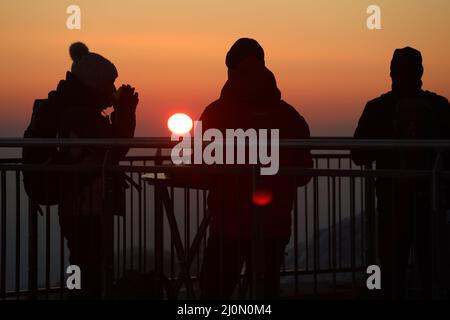 Schierke, Deutschland. 20. März 2022. Wanderer genießen den Sonnenaufgang auf dem Brocken trotz stürmischer Windböen bei kalter Luft. Bei der Tagundnachtgleiche zeigt sich die Sonne vom frühen Morgen bis zum Abend. Die Tagundnachtgleiche markiert den astronomischen Beginn des Frühlings. Quelle: Matthias Bein/dpa-Zentralbild/dpa/Alamy Live News Stockfoto