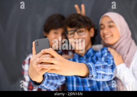Gruppe von arabischen Teenagern, die Selfie-Fotos auf dem Smartphone mit schwarzer Tafel im Hintergrund machen. Selektiver Fokus Stockfoto