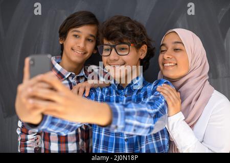 Gruppe von arabischen Teenagern, die Selfie-Fotos auf dem Smartphone mit schwarzer Tafel im Hintergrund machen. Selektiver Fokus Stockfoto