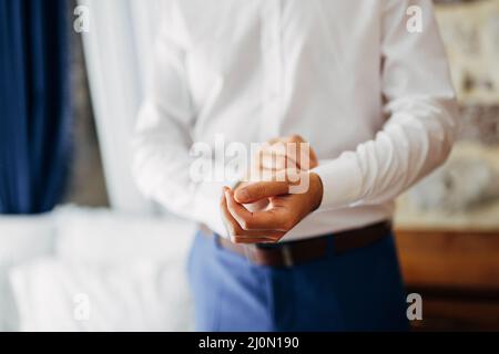 Mann in blauer Hose knöpft einen Knopf an der Manschette eines weißen Hemdes. Nahaufnahme Stockfoto