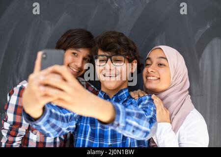 Gruppe von arabischen Teenagern, die Selfie-Fotos auf dem Smartphone mit schwarzer Tafel im Hintergrund machen. Selektiver Fokus Stockfoto