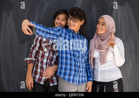 Gruppe von arabischen Teenagern, die Selfie-Fotos auf dem Smartphone mit schwarzer Tafel im Hintergrund machen. Selektiver Fokus Stockfoto