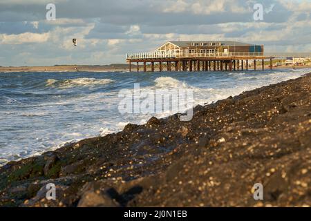 Zeeland, Holland - 27. September 2021: Strandrestaurant auf Stelzen am Abend an der Nordsee. Gebäude über dem Wasser auf dem steinigen Damm. Wasser sp Stockfoto