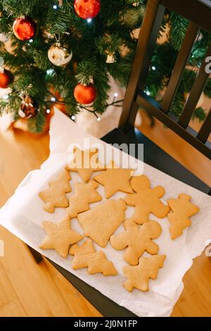 Eine Nahaufnahme eines Sets aus Fischgräten, Mann, Glocke und Inbierkeksen auf weißem Pergament zum Backen in der Nähe eines verzierten Weihnachts-T Stockfoto