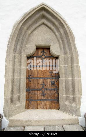 Gewölbte antike Kirche Holztür mit schwarzen Eisenornamenten in einer Steinwand. Stockfoto