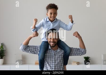 Fröhlicher kleiner afrikanischer Junge, der auf dem Nacken des Vatis sitzt Stockfoto