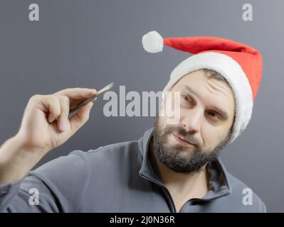 Ein bärtiger Mann in einem roten weihnachtsmann-Hut hält einen Kunstpinsel in der Hand. Santa-Künstler. Weichfokus Stockfoto